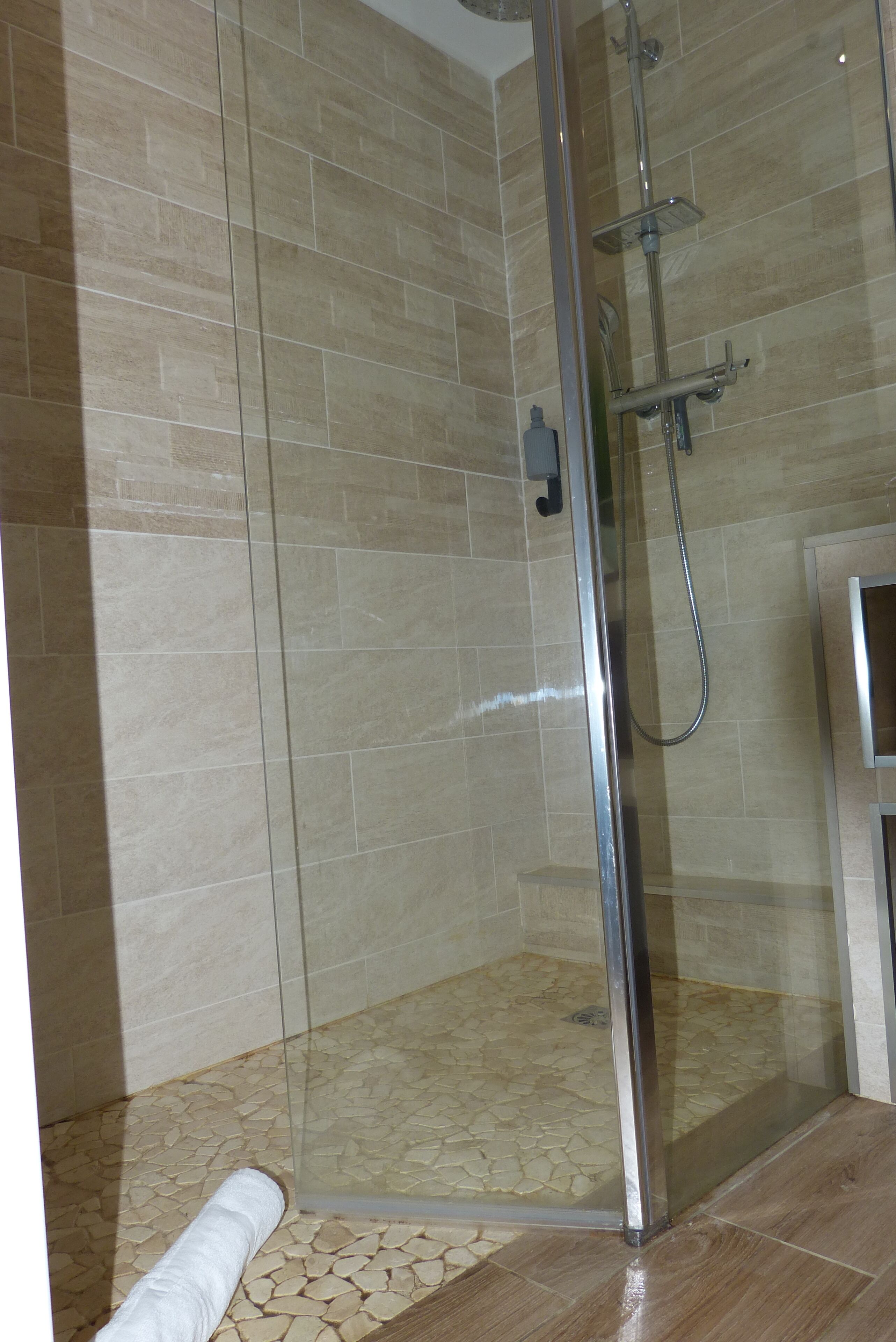 Un área de ducha con paredes de vidrio, azulejos color beige y una puerta de vidrio.