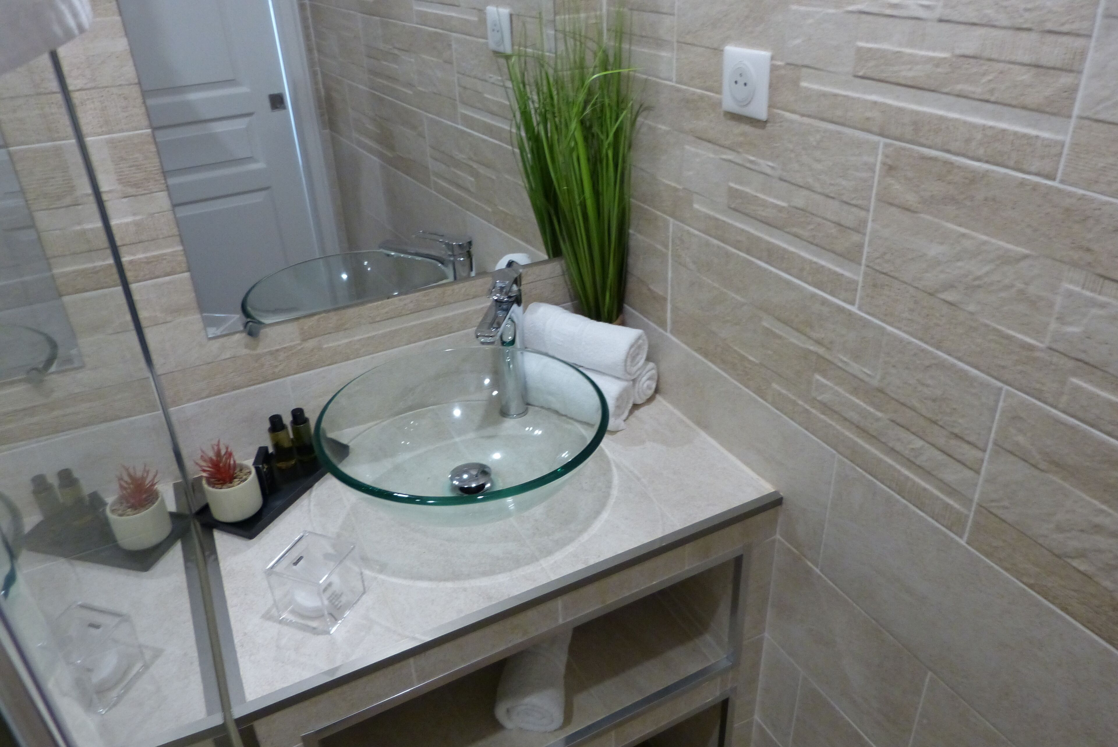 A bathroom with a glass bowl sink, a mirror, a towel rack, and a potted plant.