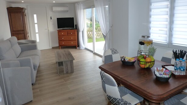 Una sala moderna con un sofá, una mesa de centro de madera, una mesa de comedor con sillas, un televisor y vistas a través de la puerta de cristal.