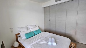 Un lit bien fait, agrémenté d’oreillers blancs et turquoise, avec une tête de lit en bois et une table de chevet en bois sur laquelle se trouve une lampe.