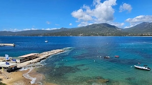 Une zone côtière caractérisée par des eaux bleues et limpides, des bateaux et une jetée rocheuse.
