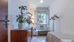 A bedroom with a bed, a dresser, a window with curtains, a plant, and a coat rack.