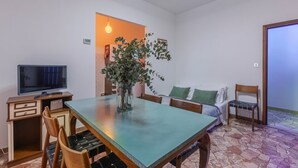 A dining area with a table, chairs, a television, a plant, and a sofa.