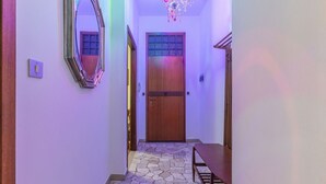 A hallway with a wooden door, a mirror, a chandelier, and a stone-patterned floor.