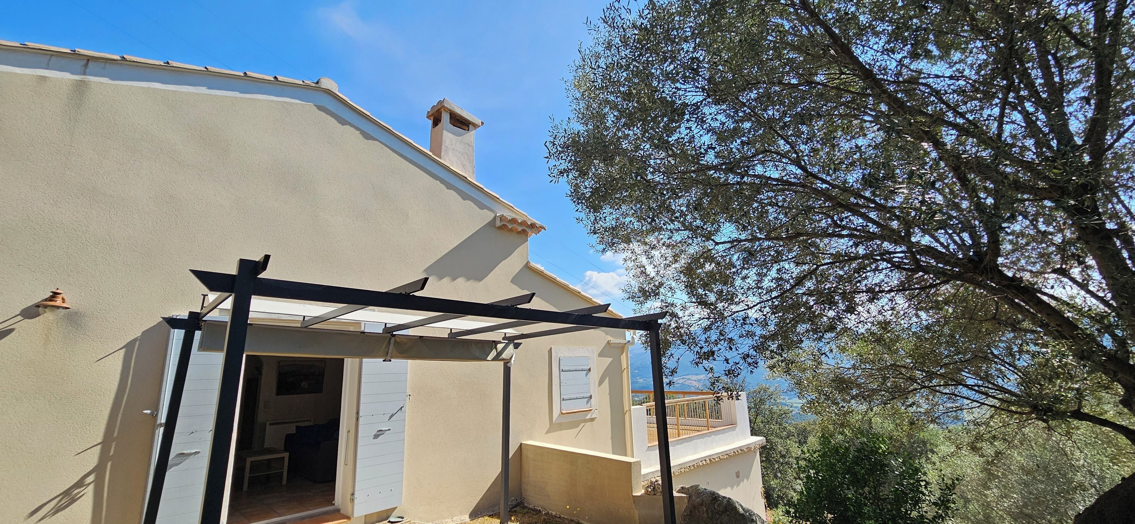 A house with a pergola structure, a visible door, and a view of a tree and landscape.