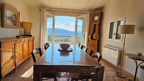 A dining area with a long table, chairs, a wooden cabinet, a clock, and a view of mountains through a glass door. - Super idyllic & antique villa with breathtaking sea view (Olmeto)