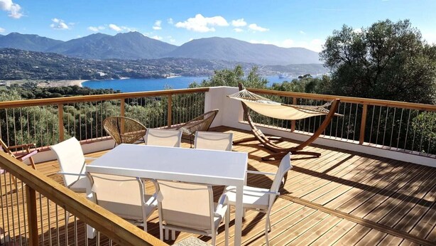 A wooden deck with a table and chairs, a hammock, and a view of mountains and a lake. - Super idyllic & antique villa with breathtaking sea view (Olmeto)