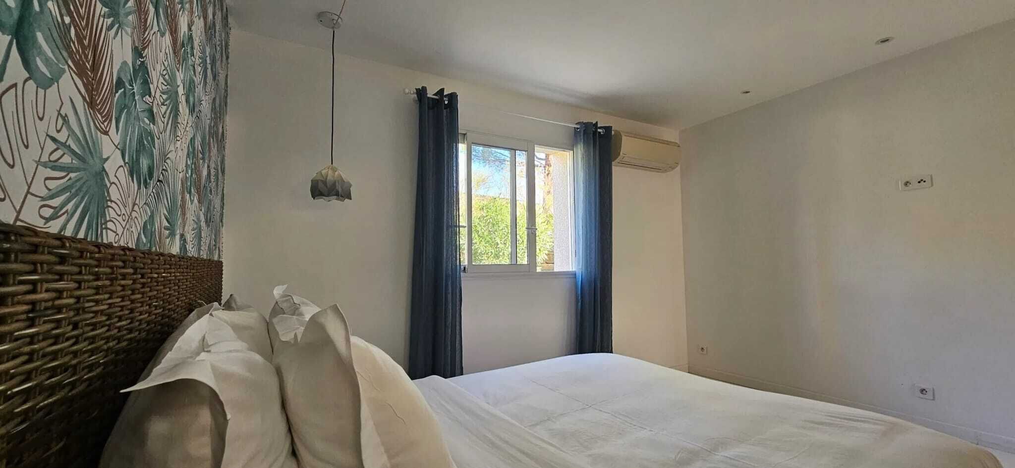 A bedroom with a bed, a window with curtains, a wall with a mural, and a hanging light fixture.