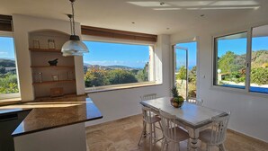 A kitchen with a dining area, large windows, and a view of the landscape. - Luxury villa Les Amandiers, sea view & swimming pool (Propriano)