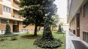 A courtyard with a large tree, smaller trees, a stone pathway, and a building with balconies.