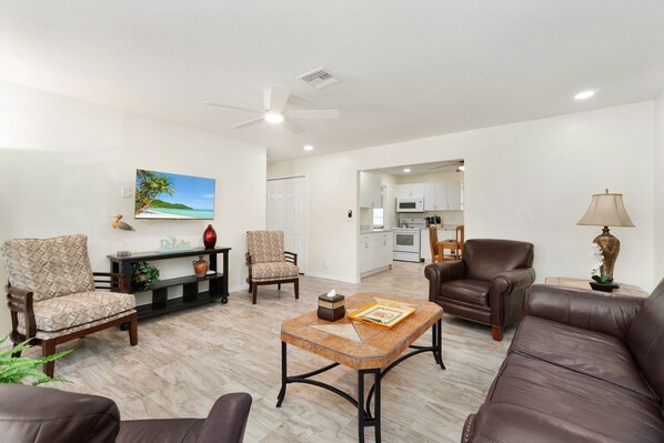 A living room with a brown leather sofa, patterned armchairs, a wooden coffee table, and a painting of a beach scene.