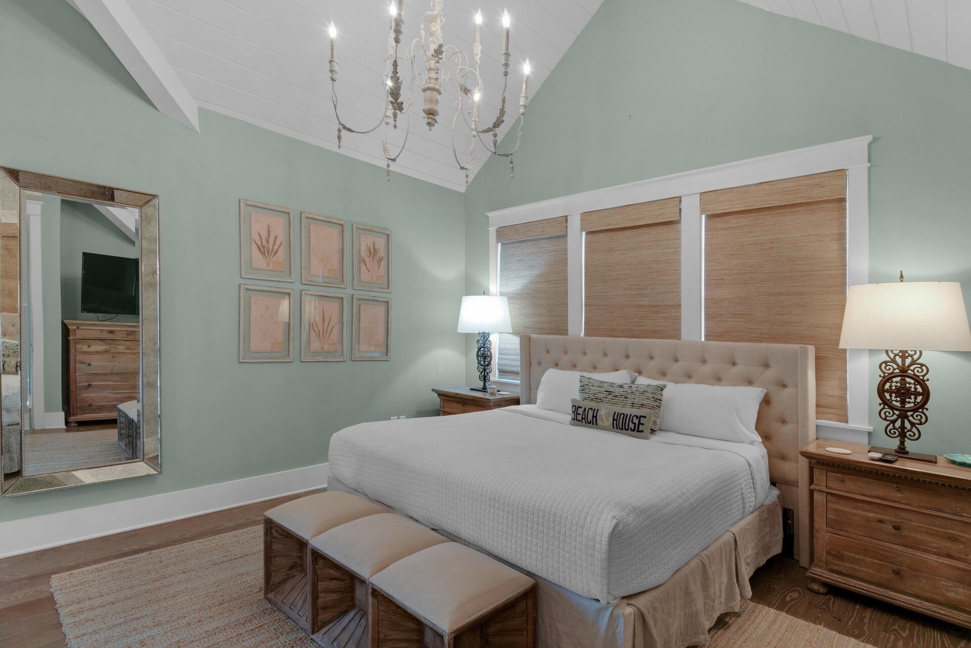 A bedroom with a large bed, a chandelier, a dresser, and a mirror.
