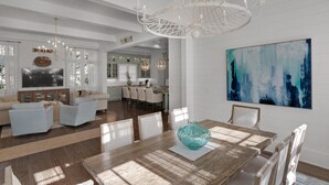 Ein geräumiges Wohnzimmer mit einem großen Esstisch, einer Küche im Hintergrund und einem modernen Kronleuchter.