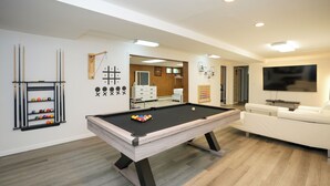 A modern living room with a pool table, a white sofa, and a billiards rack.