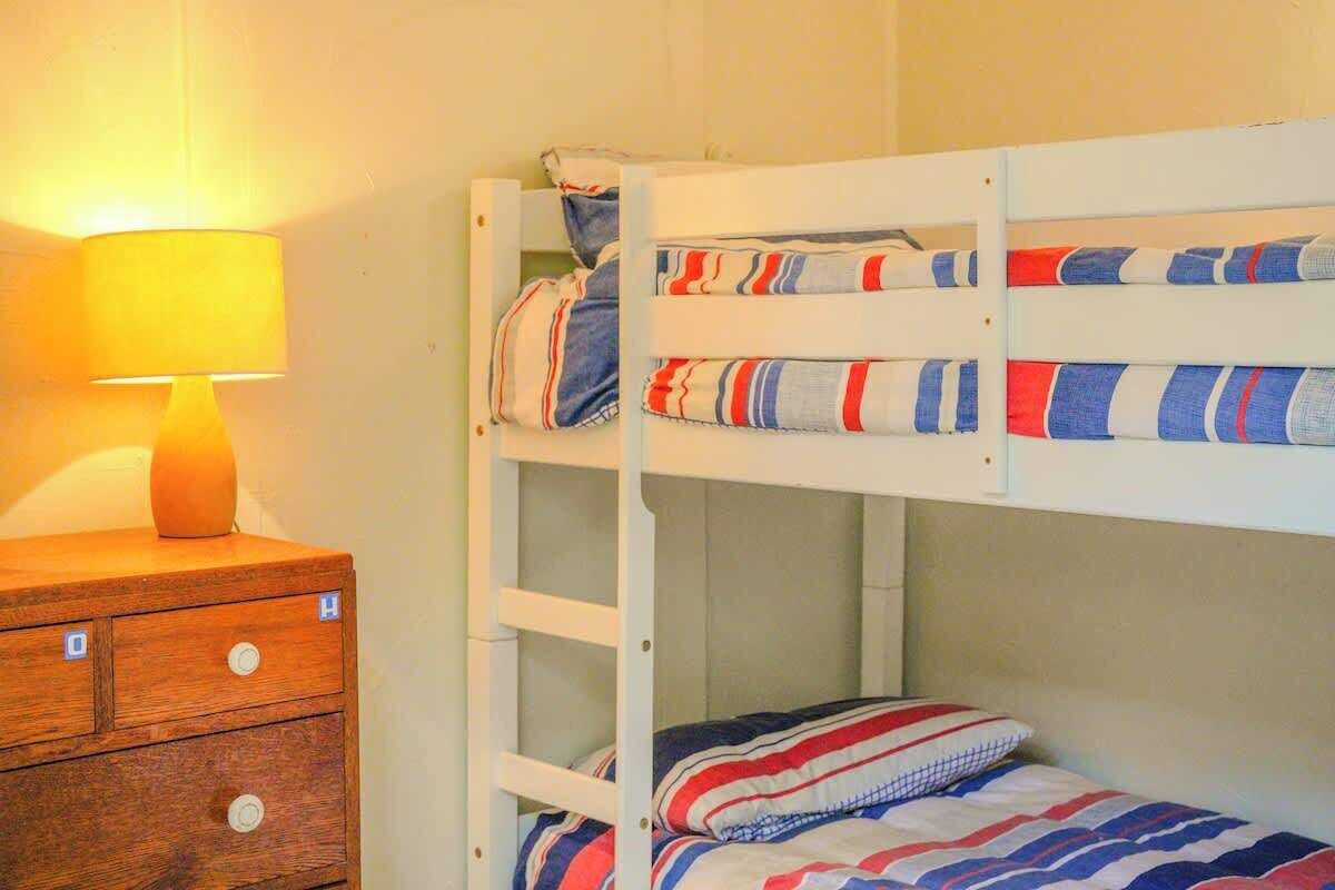 A bunk bed with striped bedding, a wooden dresser with drawers, and a lamp.
