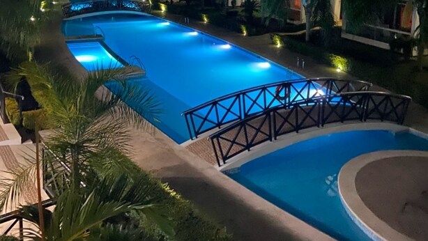 Piscina rodeada por palmeiras e edifícios modernos à noite.