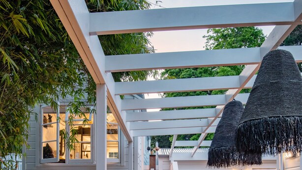 A wooden deck with a pergola, outdoor seating, and a staircase leading to an upper level.