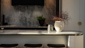 A modern kitchen with a bar area, featuring a large island, bar stools, a potted plant, and a pendant light.