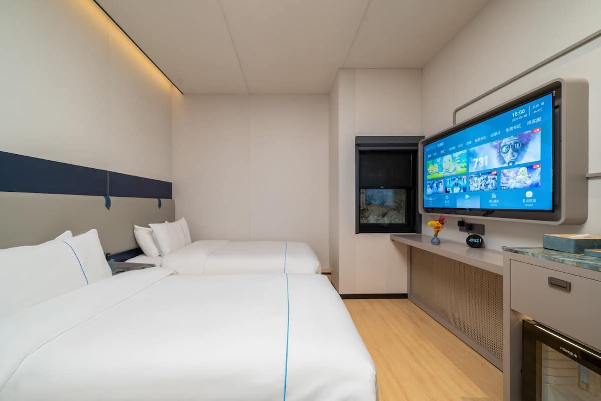Une chambre d’hôtel avec deux lits, un téléviseur à écran plat fixé au mur, une petite fenêtre et un mini-bar.