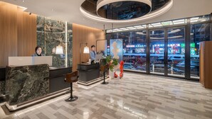 A modern hotel reception with a marble reception desk, a receptionist, and a large window offering a view of the street. - Beijing Yihai Culture Hotel (Beijing)