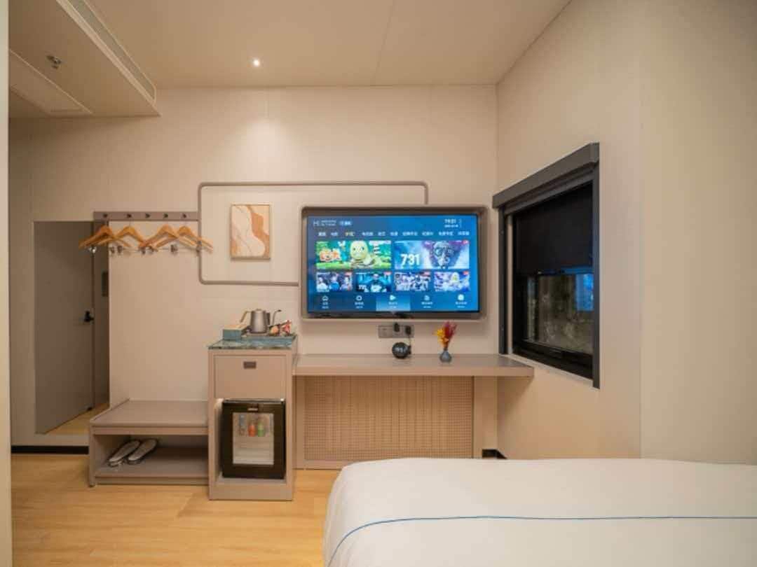 Camera d'albergo con un letto, una TV a parete, una scrivania con frigorifero e un porta scarpe.