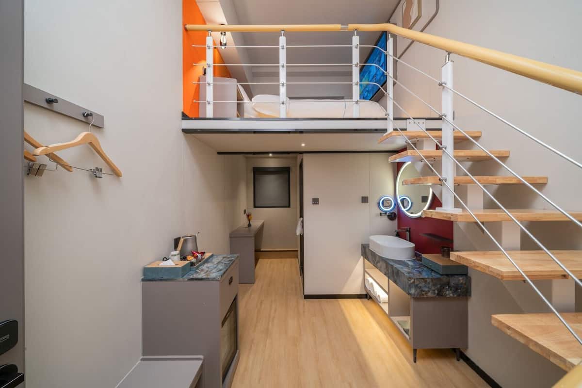 Une chambre d’hôtel moderne avec un espace nuit en mezzanine, une cuisine dotée d’un plan de travail en marbre et une salle de bain avec un meuble-lavabo et un miroir.