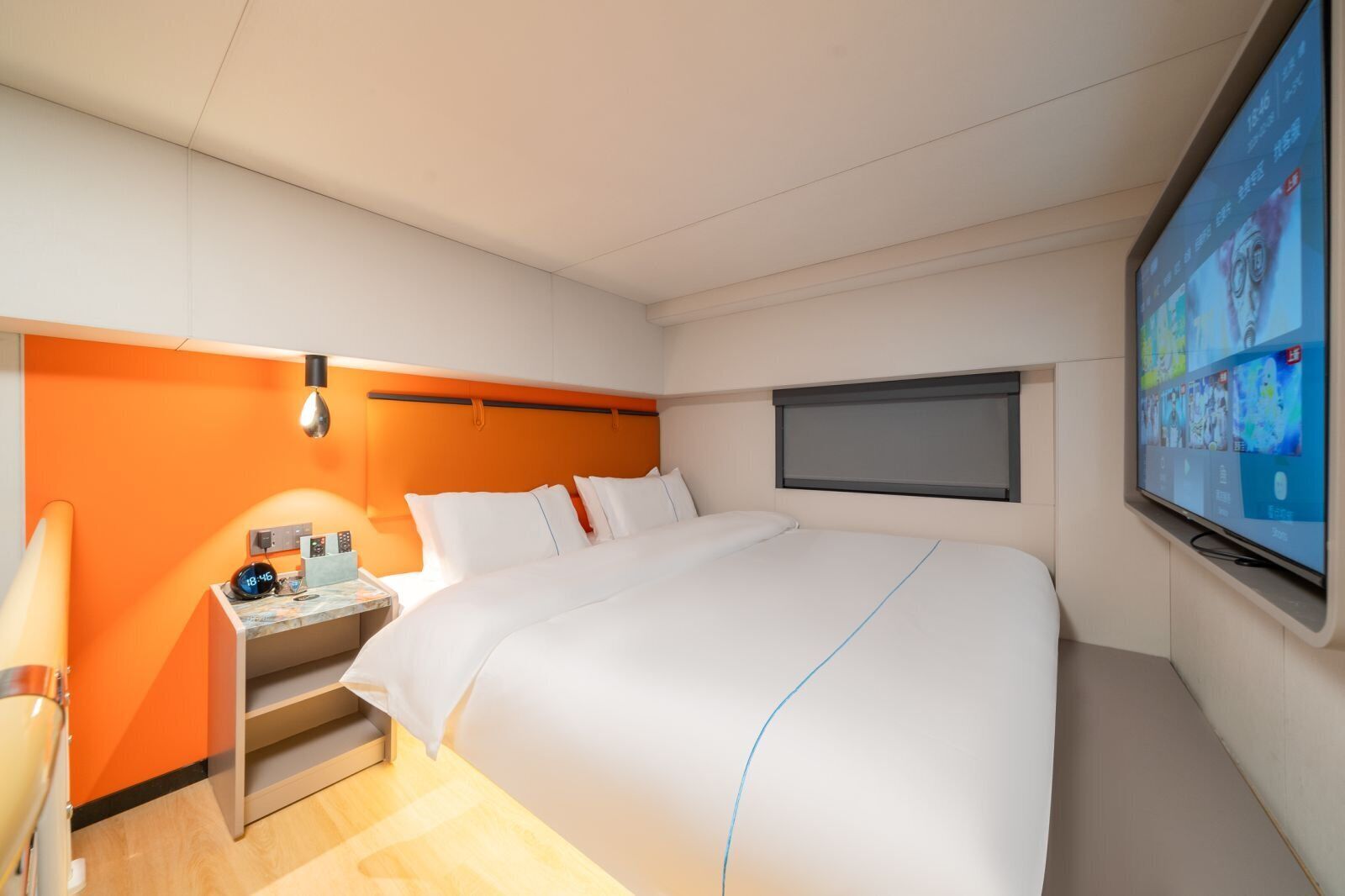 A hotel room with a bed, a desk with a lamp, a TV, and a window.
