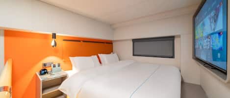 A hotel room with a bed, a desk with a lamp, a TV, and a window.