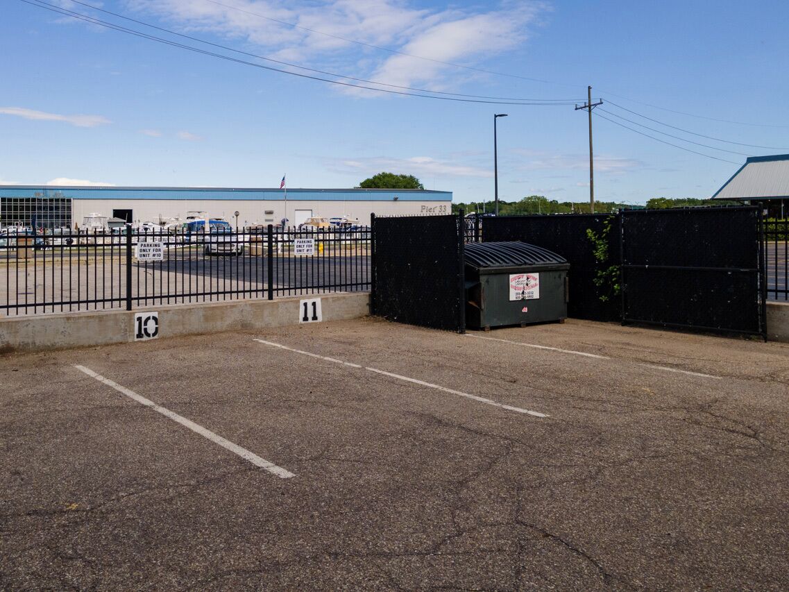 A parking lot with a fence, a building labeled "Pier 33", and a small trash bin.
