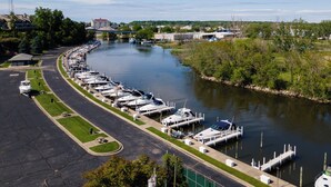 A marina with boats docked along a curved waterfront, a road adjacent to the water, and buildings in the background. - Luxury Waterfront Condo (St. Joseph)