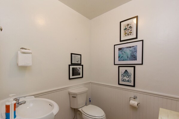 Un baño con un lavamanos blanco, inodoro y fotografías enmarcadas en la pared.