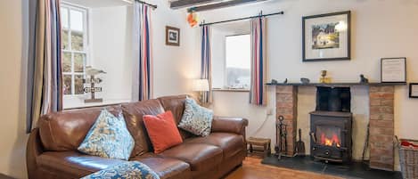 A cozy living room with a leather sofa, striped curtains, a fireplace, and a view of the outside.