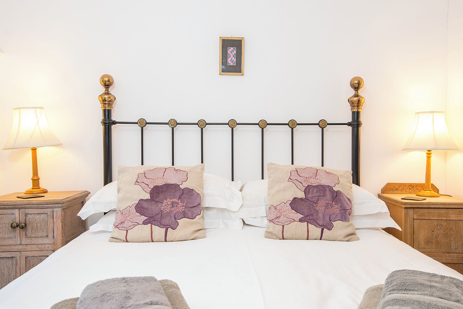 A neatly made bed with two decorative pillows, a framed picture on the wall, and two bedside lamps on wooden nightstands.