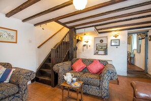 A cozy living room with a patterned sofa, a small table with a teapot and cups, a staircase, and a dining area visible through an open door. - Beach Cottage, Holiday Cottage Abereiddy, Sleeps 6, 3 bedrooms,  bathrooms (Haverfordwest)