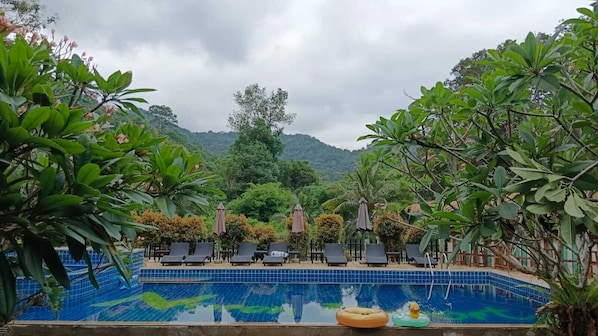 A pool with lounge chairs and umbrellas, surrounded by lush greenery and hills in the background. - Iyara Boty Resort (Ko Chang)