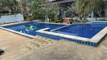A rectangular swimming pool with blue tiles, surrounded by a gravel area and various plants.