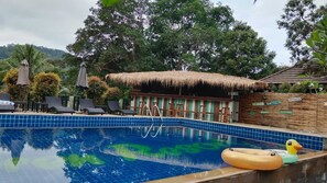 A swimming pool with lounge chairs, a thatched-roof structure, and a wooden fence with signs. - Iyara Boty Resort (Ko Chang)