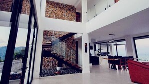 Un interior amplio con techo alto, una escalera que lleva a un nivel superior y un comedor con vistas.