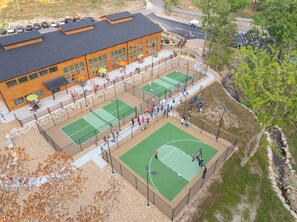 Instalación deportiva de varios niveles con canchas de tenis y un edificio con grandes ventanales.