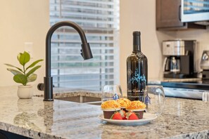A kitchen counter with a bottle of wine, two glasses, and a plate with food.