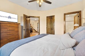 A bedroom with a bed, a dresser, and a ceiling fan. There is a sign on the wall and a door leading to another room.