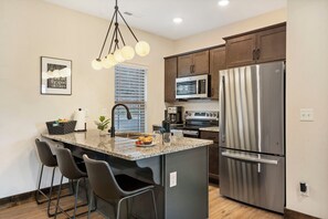 Una cocina moderna con una isla central, electrodomésticos de acero inoxidable y taburetes de bar.