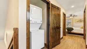 Una lavandería con lavadora y secadora, suelo de madera y una cama en la habitación contigua.