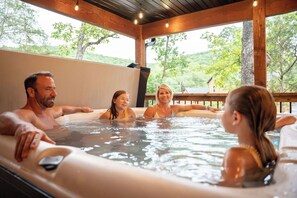 Un grupo de personas en un jacuzzi con vistas a árboles y una terraza de madera.