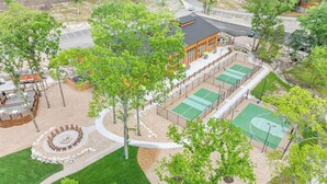 Un espacio al aire libre con una fogata, canchas de tenis y un edificio con ventanas grandes.