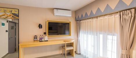 Camera d'albergo con un letto, una scrivania, una TV, un condizionatore d'aria e una finestra con tende.