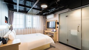 Una habitación de hotel con cama, escritorio, computadora, televisor y armario.