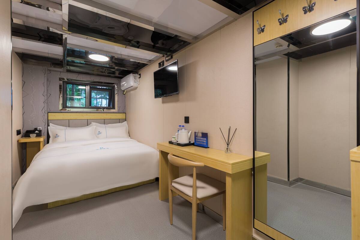 A hotel room with a bed, desk, chair, TV, and a mirror.