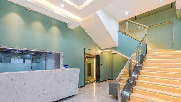 Un área de recepción con mostrador de mármol, una escalera con barandilla de cristal y un diseño interior moderno.