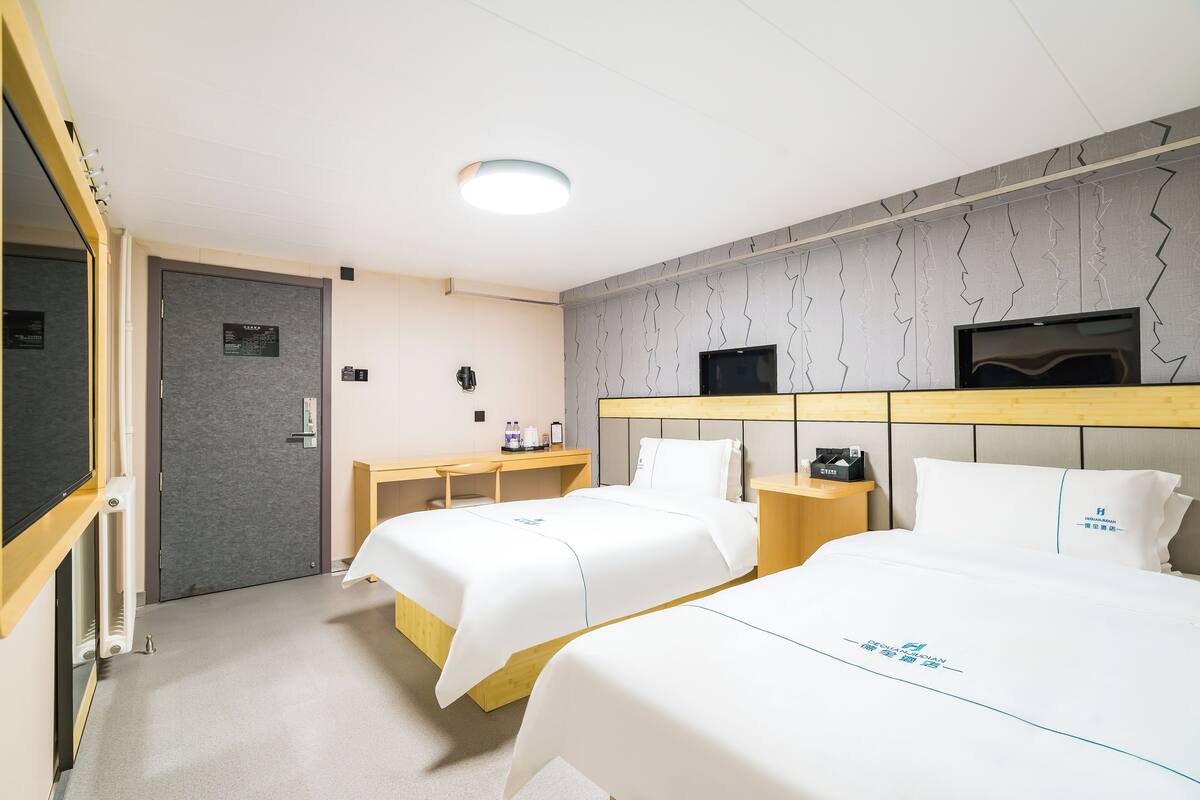 A hotel room with two beds, a desk, a TV, and a door.